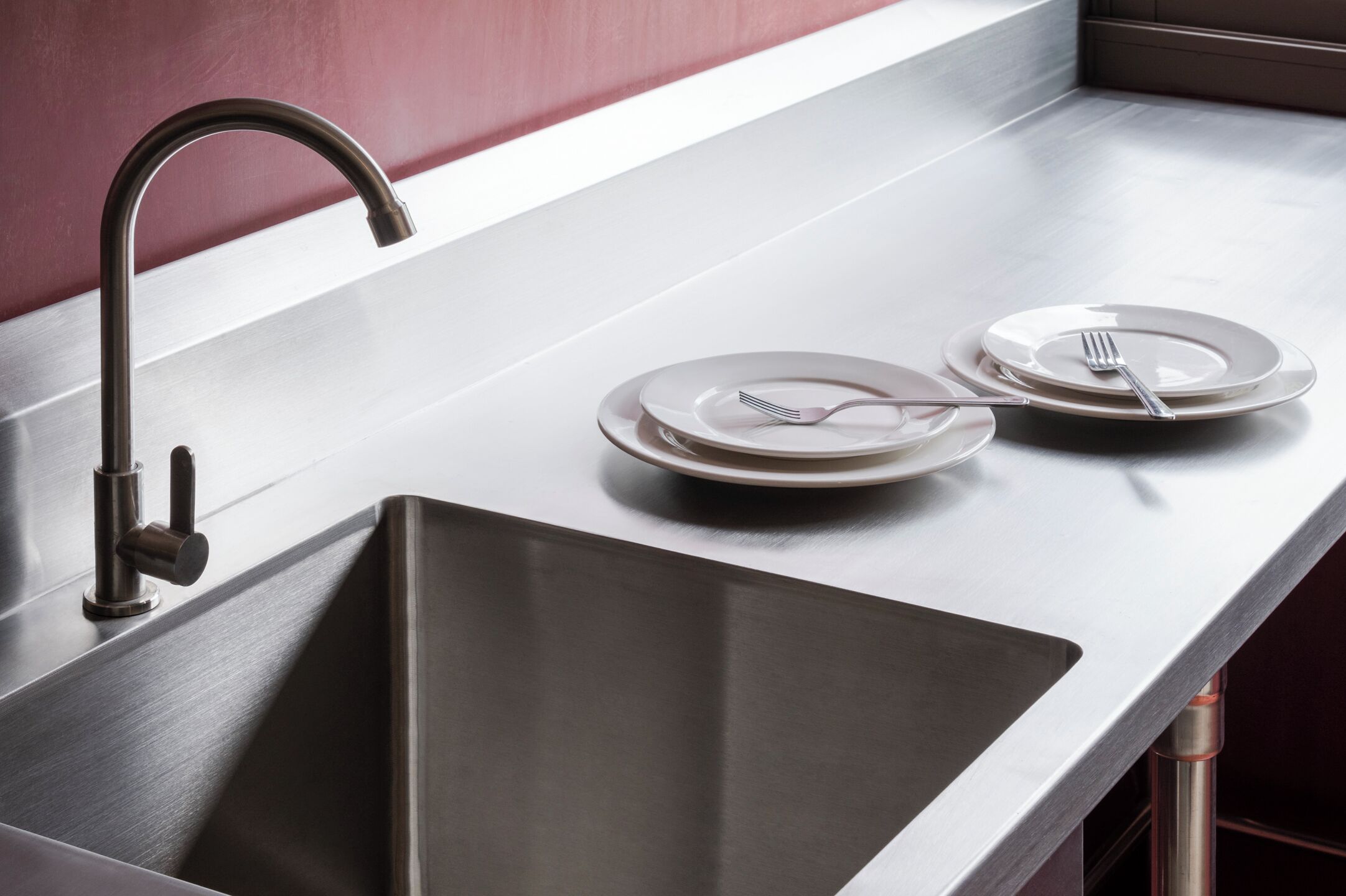 A stainless steel kitchen sink with a modern faucet, two white plates with forks, and a clean countertop.
