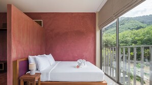 Une chambre dotée d’une grande fenêtre, d’un lit, d’une table de chevet et offrant une vue sur un paysage verdoyant et luxuriant.