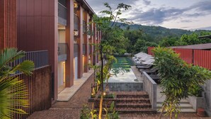 Un hôtel moderne doté d’une piscine, entouré d’une végétation luxuriante et offrant une vue sur des collines lointaines.