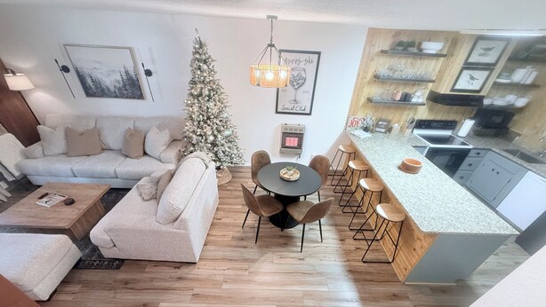 Un salon moderne avec un canapé, une table basse et un sapin de Noël. On y trouve également un coin repas avec une table ronde et des chaises, ainsi qu’une cuisine avec un comptoir et des placards.