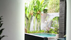 A modern outdoor pool area with a black lounge chair, surrounded by lush greenery and a stone wall. - Villa Liamax (By JB Villas) (Bali)