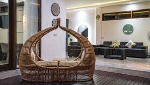 A modern interior with a unique curved wicker chair, dark sofas, and decorative wall art. - Villa Liamax (By JB Villas) (Bali)