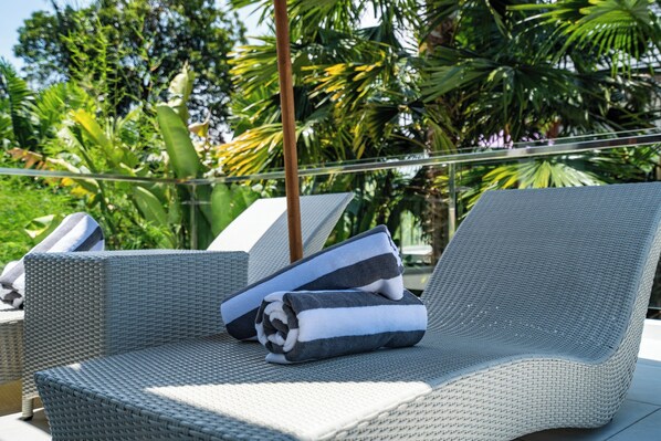 Una poltrona in vimini con un asciugamano e un cuscino, posizionata su un balcone con vista su palme.