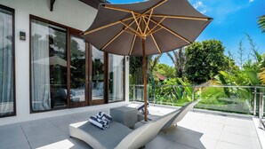 A modern outdoor seating area with a large umbrella, wicker furniture, and a glass balustrade overlooking a lush garden. - Villa Liamax (By JB Villas) (Bali)