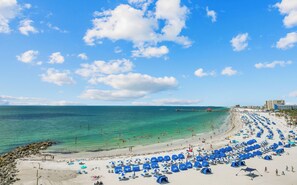 Una playa con numerosos sombrillas y carpas azules, un cielo azul despejado y un mar tranquilo.
