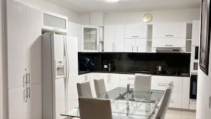 Una cocina moderna con armarios blancos, una mesa de comedor de vidrio y una encimera negra.