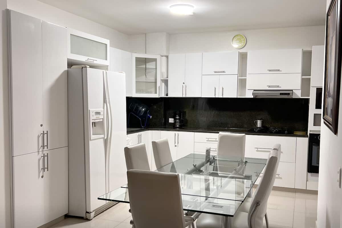A modern kitchen with white cabinetry, a glass dining table, and a black countertop.