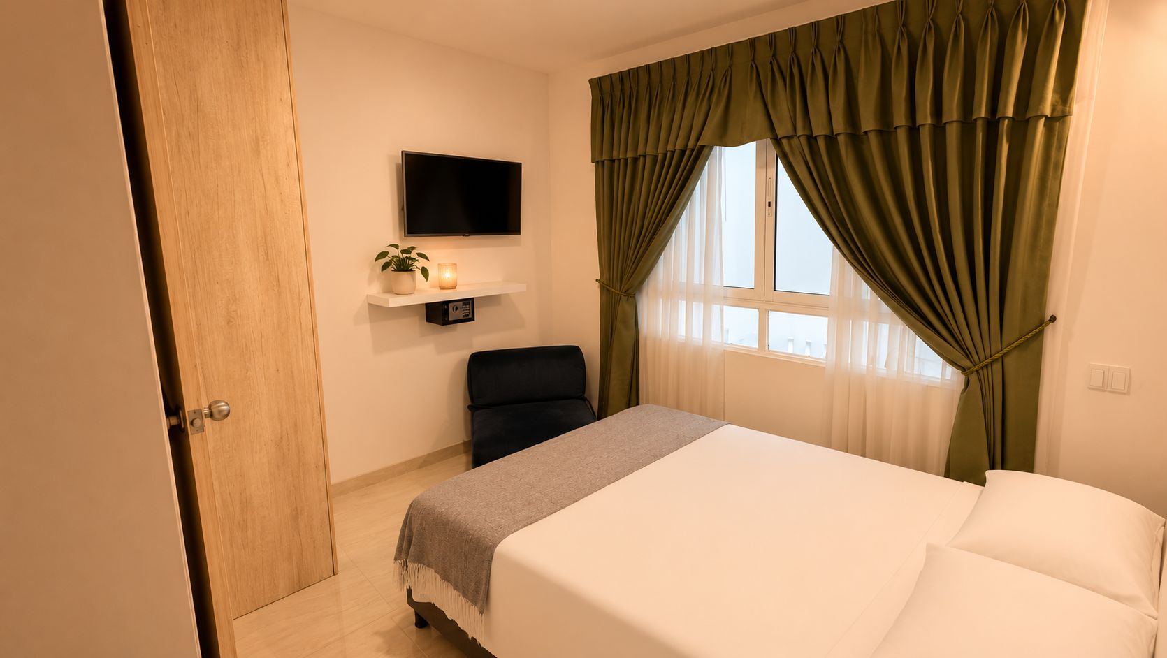 Un dormitorio con cama, una silla, un televisor en la pared y una ventana con cortinas.