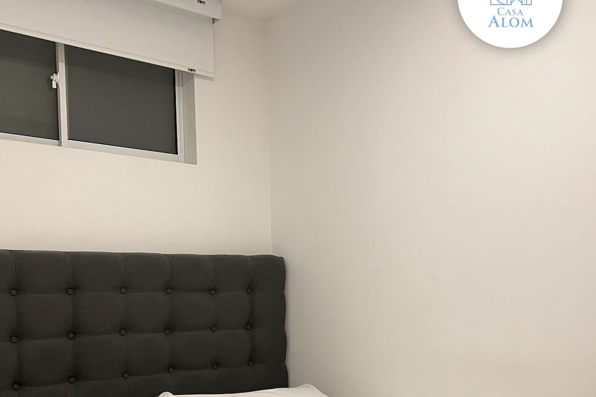 A bedroom with a dark headboard, white bedding, and a window above the bed.