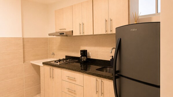 A kitchen with a black refrigerator, a gas stove, a coffee maker, and light wooden cabinets. - Casa Alom (Cali)