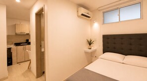 A bedroom with a bed, a bedside table with a plant, and a window above the bed. - Casa Alom (Cali)
