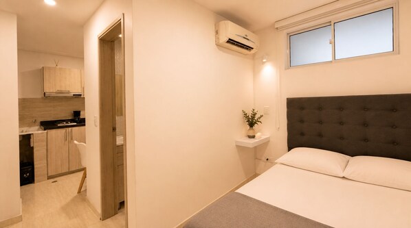 Una camera da letto con un letto, un comodino con una pianta e una finestra sopra il letto.