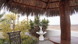 A patio with a bench, a table, a decorative fountain, and a thatched roof structure.