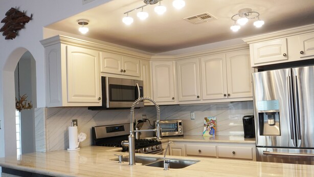 A modern kitchen with white cabinetry, stainless steel appliances, a marble countertop, and under-cabinet lighting.