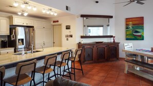 A kitchen with a large island, bar stools, a dining table, and a painting on the wall.