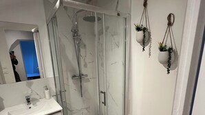 Une salle de bain moderne avec une douche à parois de verre, un meuble-lavabo blanc et deux pots de fleurs suspendus.