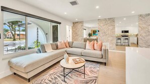 Un salon moderne doté d’un grand canapé d’angle, d’une table basse et offrant une vue sur la cuisine et l’espace extérieur.
