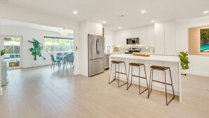 Une cuisine moderne avec des meubles blancs, un réfrigérateur en acier inoxydable et un îlot central doté de tabourets de bar.