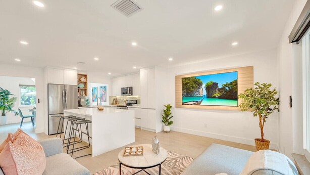 Un espace de vie moderne à aire ouverte comprenant une cuisine, un coin repas et une grande fenêtre offrant une vue sur un paysage tropical.