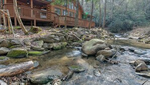 Une cabane en rondins dotée d’une terrasse donnant sur un ruisseau aux eaux tumultueuses.