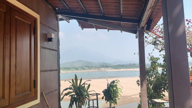 A wooden door leading to a covered outdoor area with a view of a beach and mountains. - Homestay nha go Lan Anh (Tu Vu)