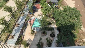 An aerial view of a property with a paved courtyard, a small building with a sloped roof, and surrounding greenery. - Homestay nha go Lan Anh (Tu Vu)