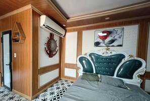 Un dormitorio con pared revestida de madera, un reloj, una cama con cabecera tapizada en verde y un aire acondicionado instalado en la pared.