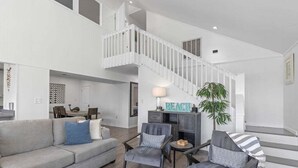 A spacious living area with a grey sofa, two armchairs, a coffee table, and a staircase leading to an upper level.