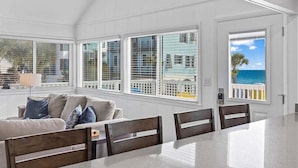 A bright room with a large window overlooking the ocean, a white ceiling, and a dining area with a table and chairs.