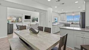 A modern kitchen with white cabinets, a large island, and a dining area with a bench.