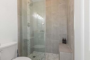 Et moderne badeværelse med en brusekabine i glas, toilet og et hyldesæt med toiletartikler.