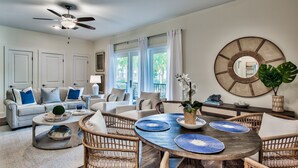 A spacious living room with a round wooden dining table, wicker chairs, and a ceiling fan.
