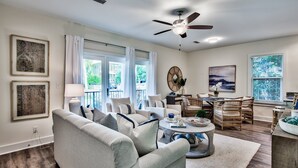 A spacious living room with a grey sofa, a round coffee table, and a dining area with wicker furniture.