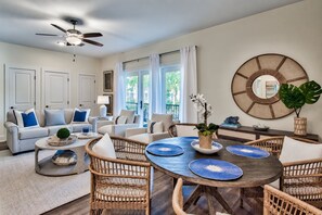 A spacious living room with a round dining table, wicker furniture, and a ceiling fan.