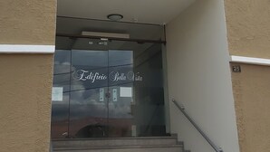 Entrada de um edifício com porta de vidro exibindo "Edificio Bella Vista" e escadas que levam para dentro.
