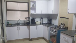 Cozinha compacta com armários brancos, fogão a gás, chaleira e cafeteira.