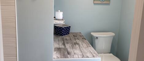 A bathroom with a wooden vanity, a toilet, and a wall-mounted shelf with a decorative item.