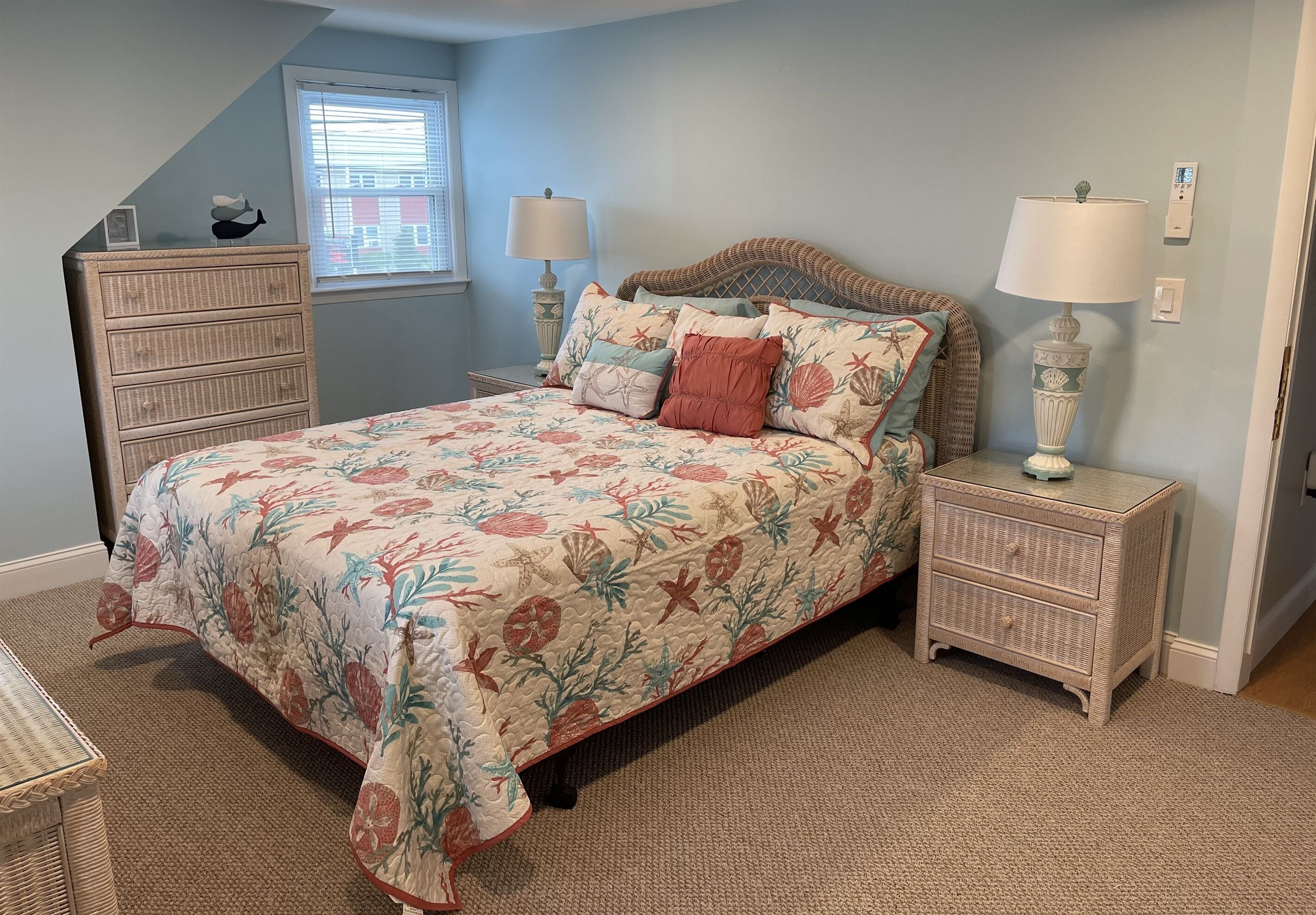 A bedroom with a floral bedspread, a dresser, two bedside tables with lamps, and a window with blinds.