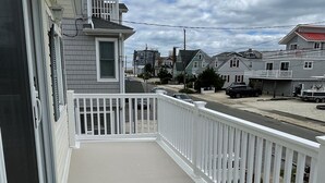 Uma varanda com guarda-corpo branco, um tapete azul com texto e vista para as casas vizinhas.