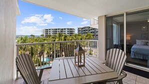A balcony with a table and chairs, a lantern, and a view of a swimming pool and buildings. - Stunning Coastal Condo | Private Beach & Water Views | Daily VIP Excursions (Fort Walton Beach)