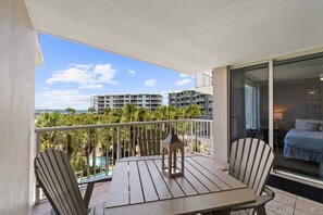 A balcony with a table and chairs, a lantern, and a view of a swimming pool and buildings.