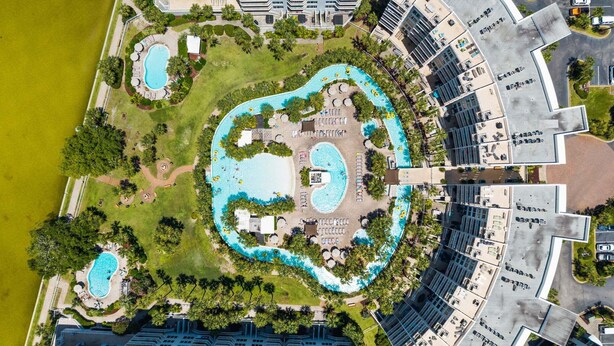 An aerial view of a resort with multiple swimming pools, lush greenery, and modern hotel buildings. - Stunning Coastal Condo | Private Beach & Water Views | Daily VIP Excursions (Fort Walton Beach)