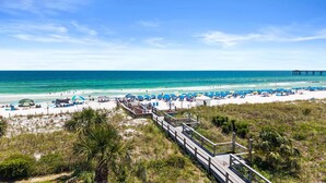 A beach with a wooden boardwalk leading to the shore, clear blue water, and a pier in the distance. - Stunning Coastal Condo | Private Beach & Water Views | Daily VIP Excursions (Fort Walton Beach)