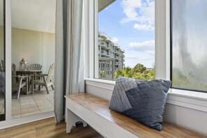 A room with a bench, a table, and chairs, a large window with a view of a building and greenery.