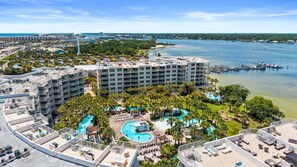 A hotel with multiple floors, a central swimming pool, and a marina in the background.