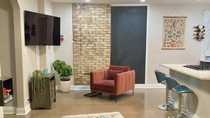 A modern living room with a flat-screen TV, a stone accent wall, a red armchair, a green sofa, and a bar area with stools.
