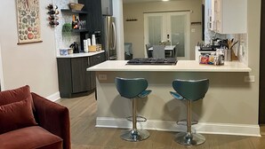 A modern kitchen with a central island, bar stools, a red sofa, and a dining area with a table and chairs.