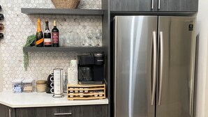 A kitchen with a stainless steel refrigerator, dark wooden cabinets, a coffee station, and a hexagonal tile backsplash.