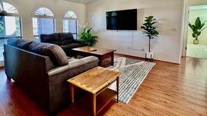 A spacious living room with a ceiling fan, a flat-screen TV mounted on the wall, and a large window with a view of the outdoors. - Spacious Prescott Home w/Fenced Yard & Central Loc (Prescott)