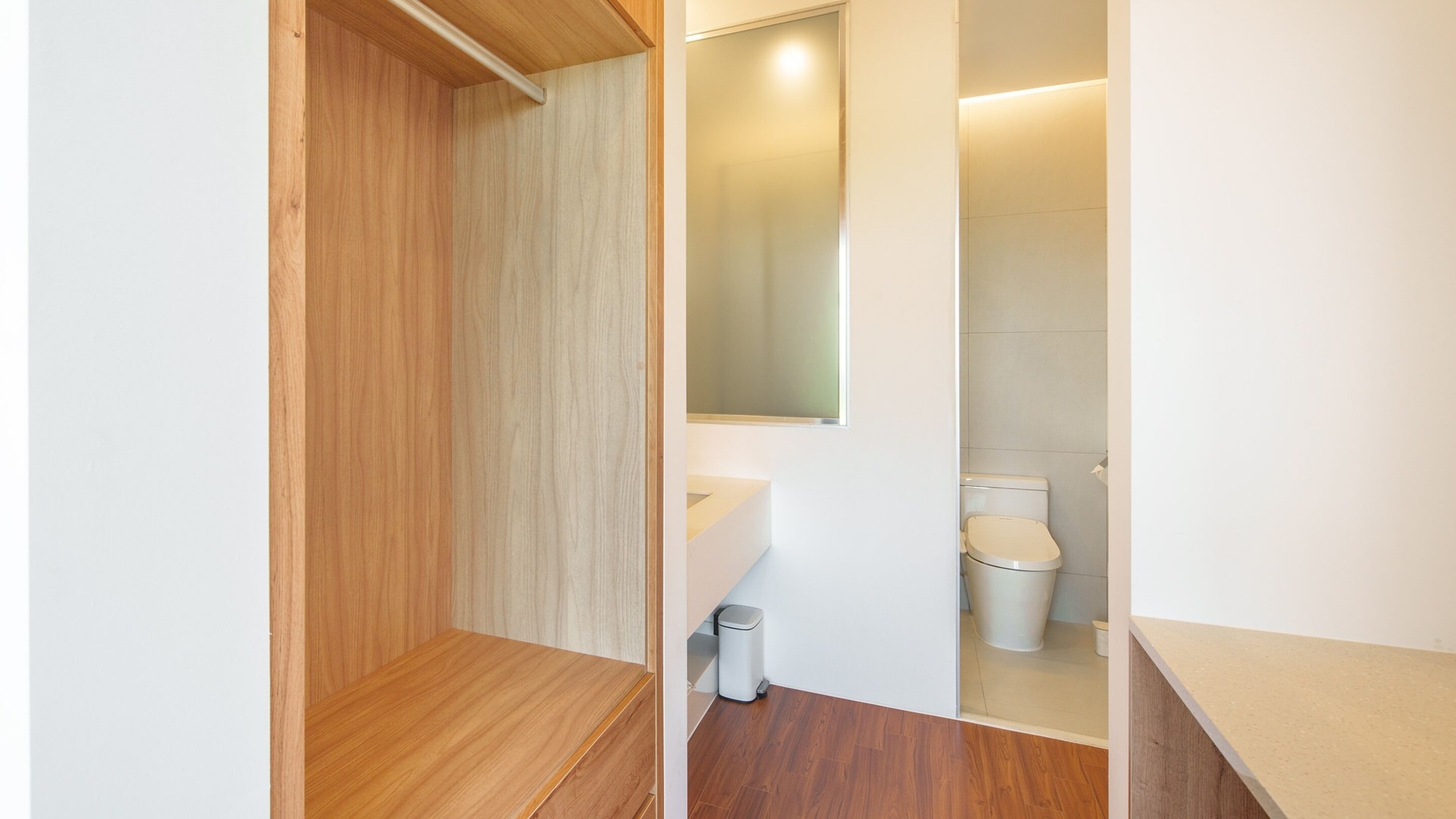 Un baño moderno con tocador de madera, inodoro y un cubo de basura.